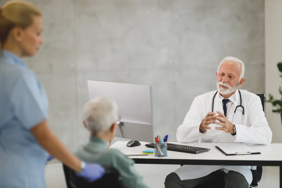 A doctor at his desk speaking with a nurse and a patient